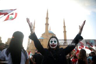 TOPSHOT - A Lebanese demonstrator, her face painted as DC comic book and film character "The Joker", takes part in a protest in the capital Beirut's downtown district's Martyr's Square on October 19, 2019. - Tens of thousands of Lebanese people took to the streets today for a third day of protests against tax increases and alleged official corruption despite several arrests by security forces. (Photo by Patrick BAZ / AFP) (Photo by PATRICK BAZ/AFP via Getty Images)