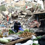 TOPSHOT - Residents buy vegetables from an ambulant vendor stationed amid the destruction in the neighbourhood of Shiyah in Beirut's southern suburbs on November 28, 2024, a day after a ceasefire between Israel and Hezbollah took effect. Since the ceasefire took effect on November 27, tens of thousands of Lebanese who fled their homes headed back to their towns, neighbourhoods and villages, only to find scenes of devastation. (Photo by IBRAHIM AMRO / AFP) (Photo by IBRAHIM AMRO/AFP via Getty Images)