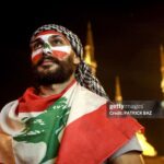 TOPSHOT - A man wearing facepaint in the colours of the Lebanese national flag and draped in a flag attends a demonstration at the Martyrs' Square in the centre of the capital Beirut on October 26, 2019, the Mohammed al-Amin mosque seen behind, on the tenth day of country-wide protests against tax increases and official corruption. (Photo by Patrick BAZ / AFP) (Photo by PATRICK BAZ/AFP via Getty Images)
