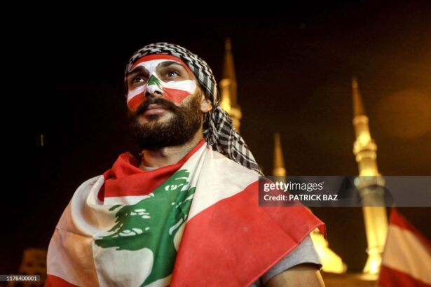 TOPSHOT - A man wearing facepaint in the colours of the Lebanese national flag and draped in a flag attends a demonstration at the Martyrs' Square in the centre of the capital Beirut on October 26, 2019, the Mohammed al-Amin mosque seen behind, on the tenth day of country-wide protests against tax increases and official corruption. (Photo by Patrick BAZ / AFP) (Photo by PATRICK BAZ/AFP via Getty Images)